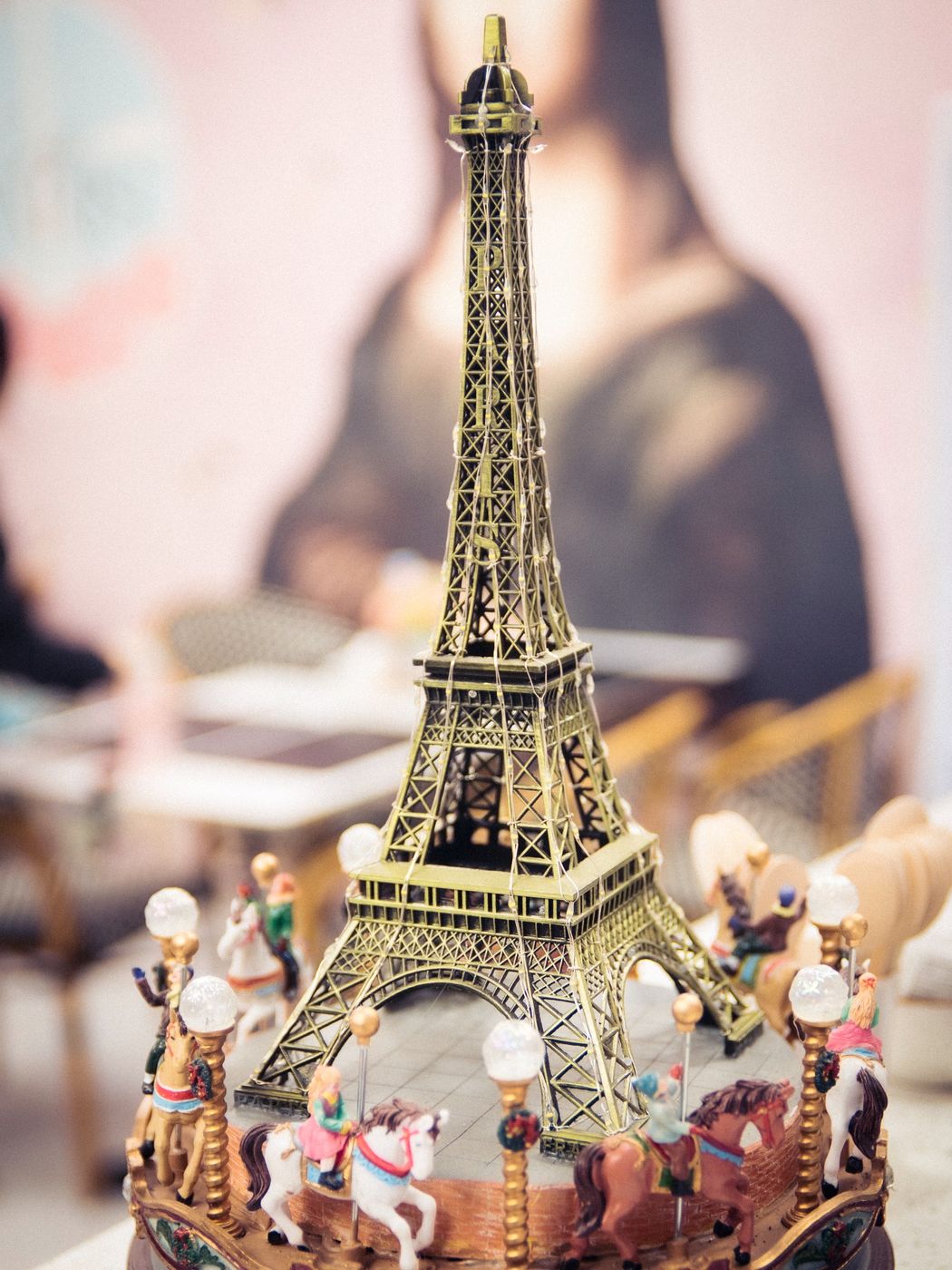 Torre Eiffel en miniatura sobre un carrusel de juguete, con la Mona Lisa al fondo, en Café París